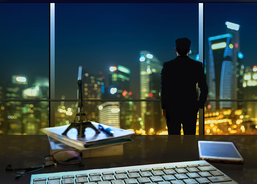 Man standing over nighttime city with keyboard and phone showing on desk